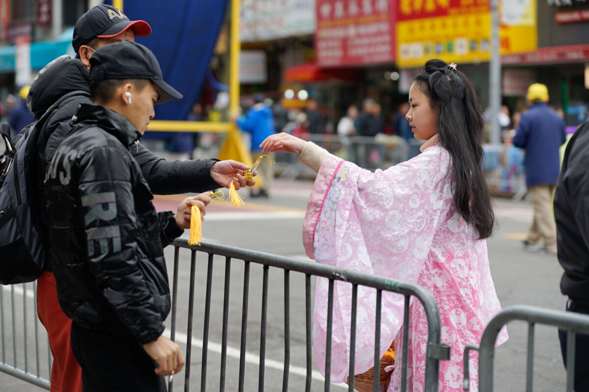Một học viên Pháp Luân Công tặng quà lưu niệm tại một cuộc diễn hành kêu gọi chấm dứt cuộc đàn áp đức tin của họ ở Trung Quốc, tại khu Flushing của Queens, New York, hôm 21/04/2024. (Ảnh: Chung I Ho/The Epoch Times)