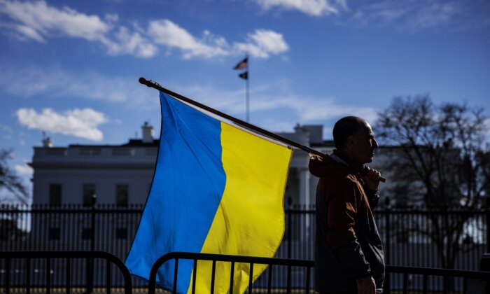 Một người đàn ông mang theo cờ Ukraine đứng trên Đại lộ Pennsylvania trước Tòa Bạch Ốc khi những người biểu tình tụ tập để phản đối cuộc xâm lược của Nga ở Thủ đô Hoa Thịnh Đốn, vào ngày 25/02/2022 (Ảnh: Samuel Corum/Getty Images)