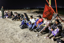 Những người nhập cư bất hợp pháp chờ để được các nhân viên Tuần tra biên giới giải quyết thủ tục sau khi vượt biên từ Mexico, với hàng rào biên giới Hoa Kỳ-Mexico ở phía sau, ở Yuma, Arizona, vào ngày 23/05/2022. (Ảnh: Mario Tama/Getty Images)
