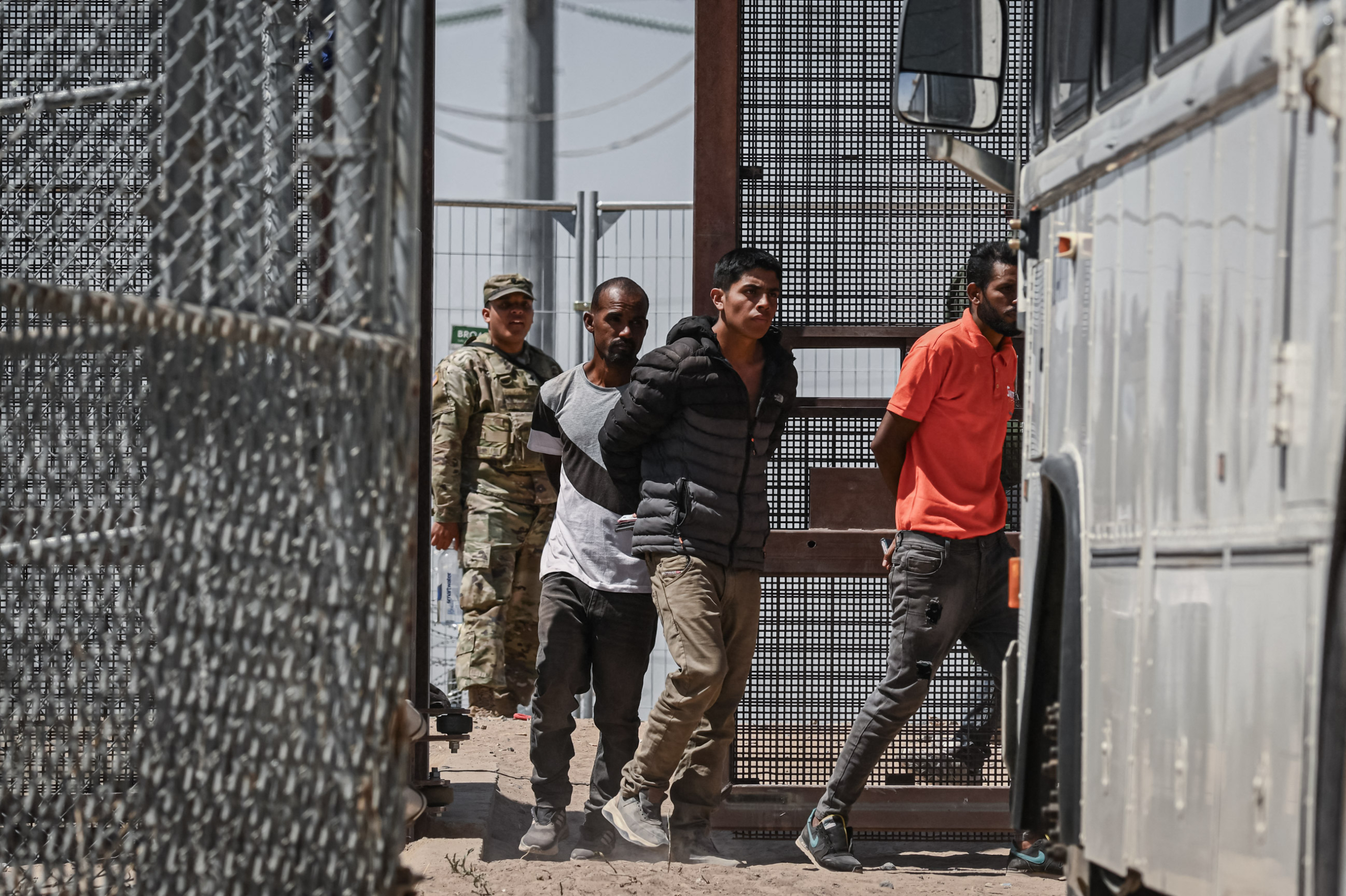 Lực lượng Vệ binh Quốc gia Texas theo dõi những người nhập cư bất hợp pháp lên xe buýt sau khi họ đầu hàng các nhân viên Tuần tra Biên giới ở biên giới Hoa Kỳ-Mexico, ở El Paso, Texas, vào ngày 12/05/2023. (Ảnh: Patrick T. Fallon/AFP qua Getty Images)