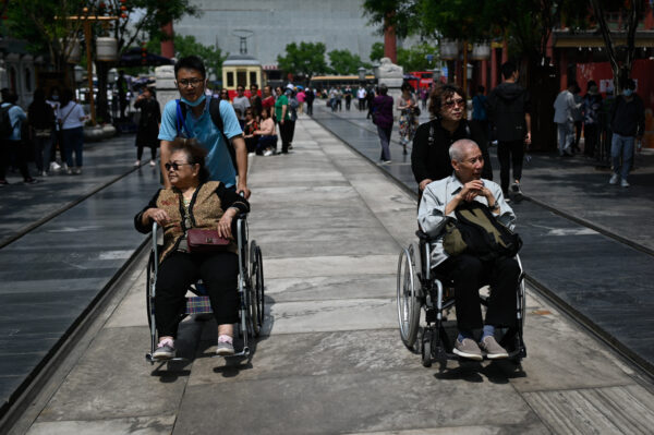 Một người đàn ông và một phụ nữ lớn tuổi được đẩy trên xe lăn dọc một con phố ở Bắc Kinh hôm 11/05/2021. (Ảnh: Wang Zhao/AFP qua Getty Images)