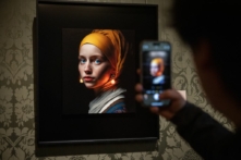Một du khách dùng điện thoại di động để chụp một hình ảnh (giữa) được thiết kế bằng trí tuệ nhân tạo bởi nhà sáng tạo kỹ thuật số Julian van Dieken sống tại Berlin, lấy cảm hứng từ bức tranh “Cô gái đeo bông tai ngọc trai” của họa sỹ Johannes Vermeer tại bảo tàng Mauritshuis ở La Haye (The Hague), vào ngày 09/03/2023. (Ảnh: Simon Wohlfahrt/AFP qua Getty Images)