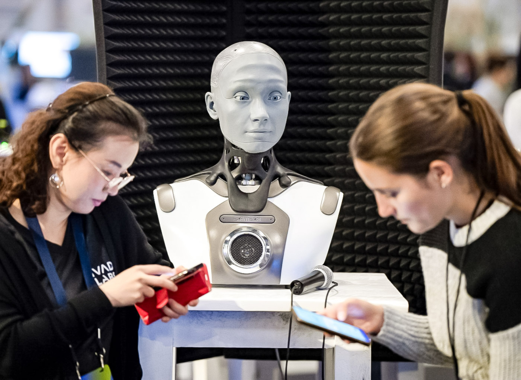 Mọi người kiểm tra điện thoại khi AMECA, một robot AI, đang theo dõi hội nghị trí tuệ nhân tạo All In tại Montreal, vào ngày 28/09/2023. (Ảnh: Ryan Remiorz /The Canadian Press)