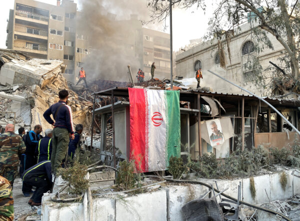 Quốc kỳ Iran treo lơ lửng trong bối cảnh khói bốc lên sau cuộc tấn công của Israel vào tòa nhà gần đại sứ quán Iran ở Damascus, Syria hôm 01/04/2024. (Ảnh: Firas Makdesi/REUTERS)