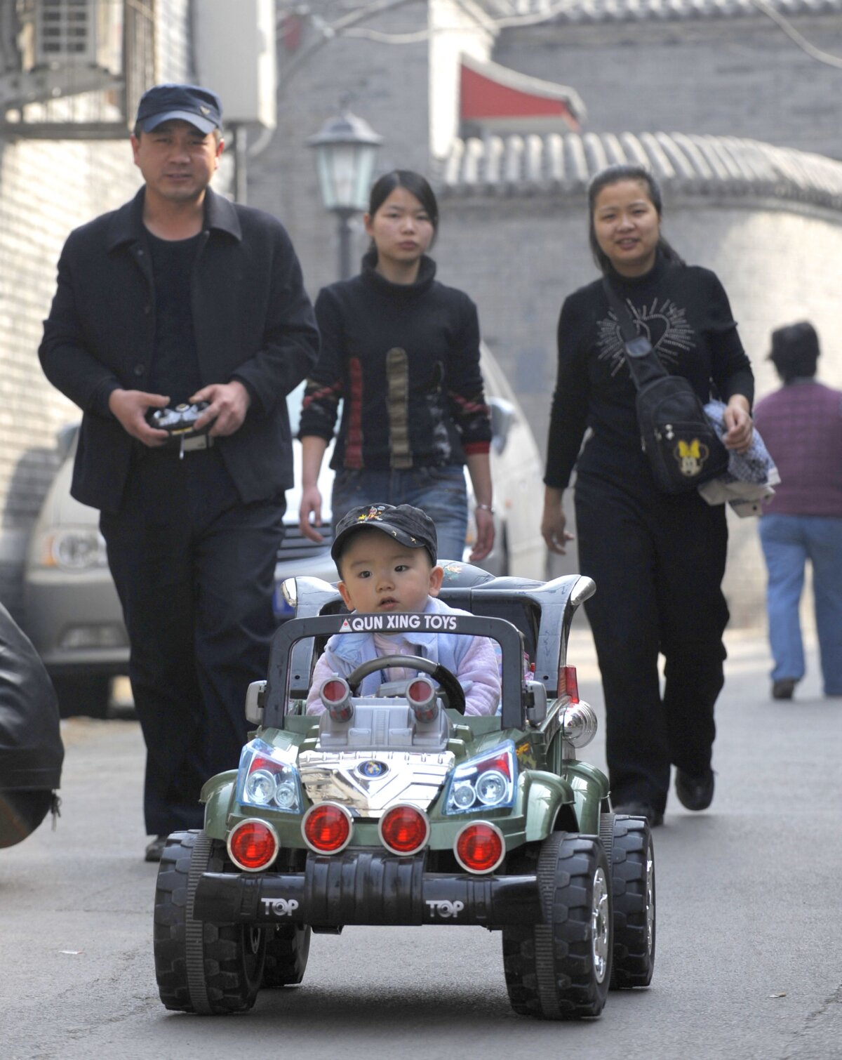 Một cậu bé ngồi trong chiếc xe hơi đồ chơi sang trọng, đi bên cạnh gia đình dọc theo một con phố ở Bắc Kinh, ngày 21/10/2011. (Ảnh: Liu Jin/AFP qua Getty Images)