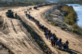 Một đoàn hơn 1,000 người nhập cư bất hợp pháp đi về phía trung tâm giải quyết tại chỗ của Lực lượng Tuần tra Biên giới Hoa Kỳ sau khi họ vượt qua Rio Grande từ Mexico vào Eagle Pass, Texas, vào ngày 18/12/2023. (Ảnh: John Moore/Getty Images)