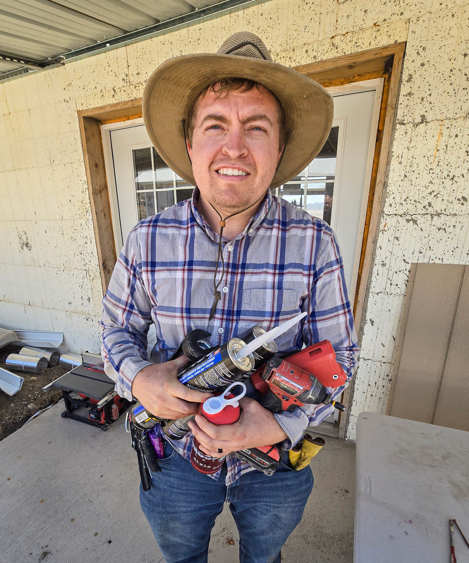 Anh Tyler Ellingson ôm theo một mớ công cụ khi làm việc tại ngôi nhà được lắp đặt thiết bị phát quang năng của mình tại cộng đồng Chiến dịch Tự lực Cánh sinh ở phía nam Utah, hôm 28/06/2024. (Ảnh: Allan Stein/The Epoch Times)