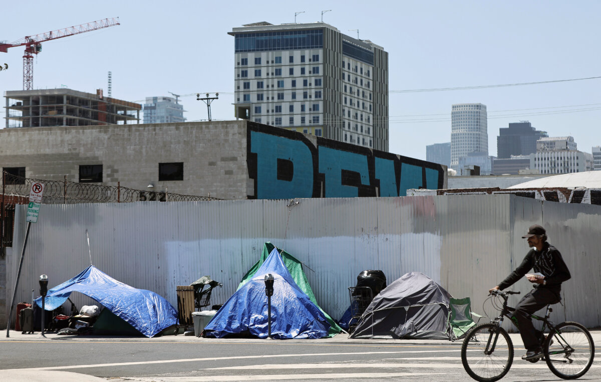 Một người đi xe đạp ngang qua các lều trại của những người vô gia cư trong cộng đồng Skid Row ở Los Angeles, hôm 28/06/2024. (Ảnh: Mario Tama/Getty Images)