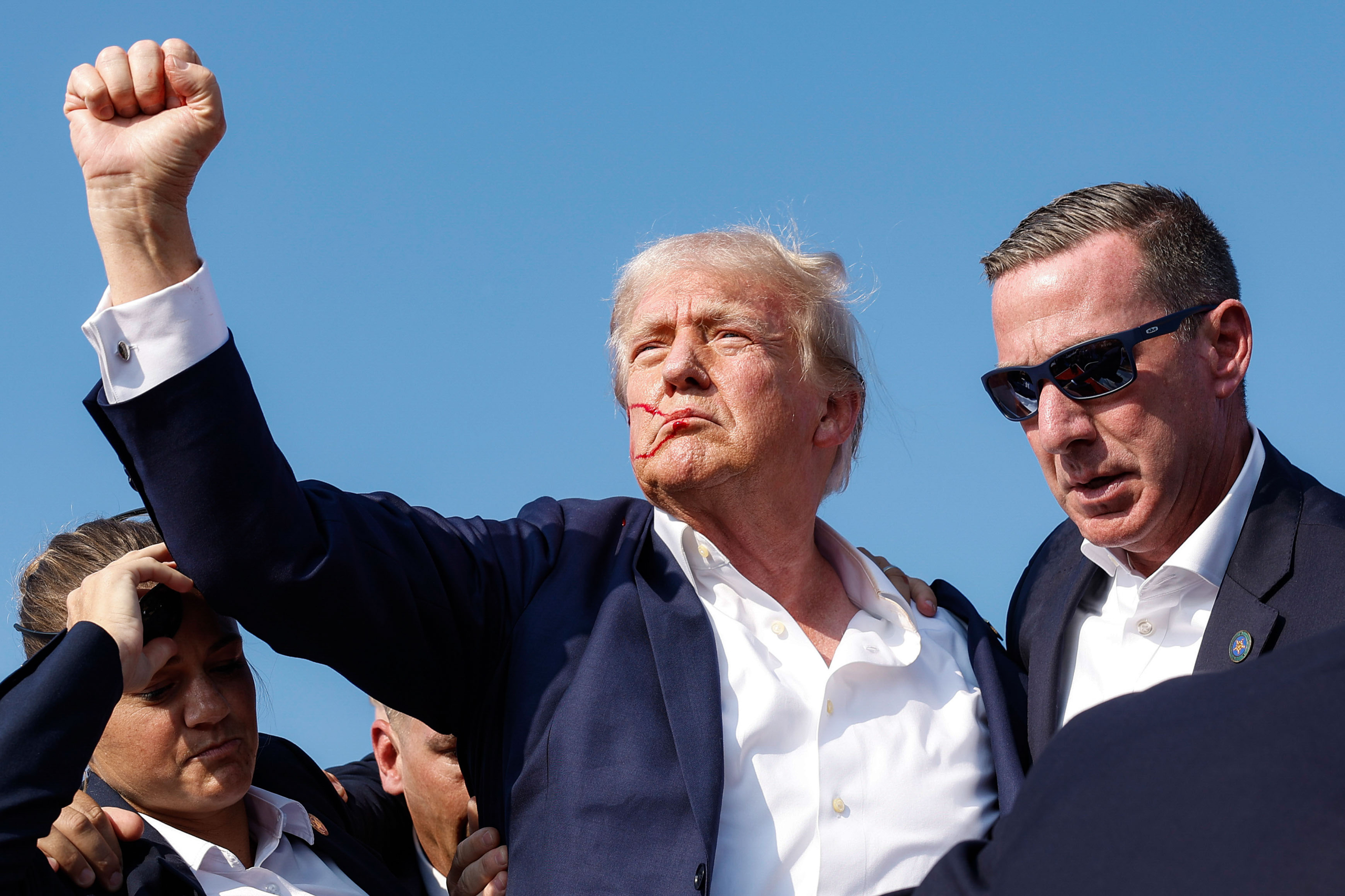 Cựu Tổng thống Trump giơ nắm tay trong lúc được gấp rút đưa ra khỏi sân khấu giữa cuộc vận động. (Ảnh: Anna Moneymaker/Getty Images)