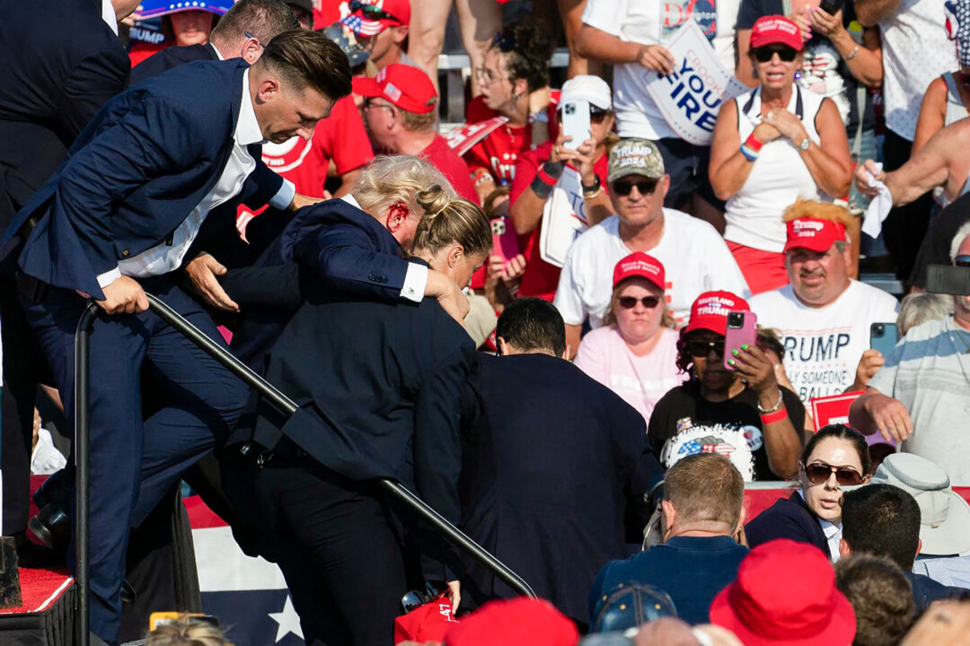 Ứng cử viên Đảng Cộng Hòa Donald Trump với vết máu trên mặt được các nhân viên mật vụ bao quanh khi ông được đưa ra khỏi sân khấu tại một sự kiện tranh cử tại Butler Farm Show Inc. ở Butler, Pennsylvania, hôm 13/07/2024. (Ảnh: Rebecca Droke/AFP qua Getty Images)