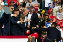 Cựu Tổng thống Donald Trump, ứng cử viên bên Đảng Cộng Hòa, với vết máu trên mặt, đang được các nhân viên mật vụ vây quanh trong khi hộ tống ông ra khỏi sân khấu tại một sự kiện tranh cử ở Butler Farm Show Inc. tại Butler, Pennsylvania, hôm 13/07/2024. (Ảnh: Rebecca Droke/ AFP qua Getty Images)