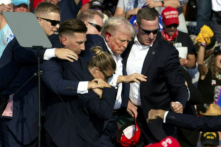 Cựu Tổng thống Donald Trump với vết máu trên mặt được các nhân viên Sở Mật vụ vây quanh khi ông được đưa ra khỏi sân khấu tại một sự kiện tranh cử ở Butler, Pennsylvania, hôm 13/07/2024. (Ảnh: Rebecca Droke/AFP qua Getty Images)
